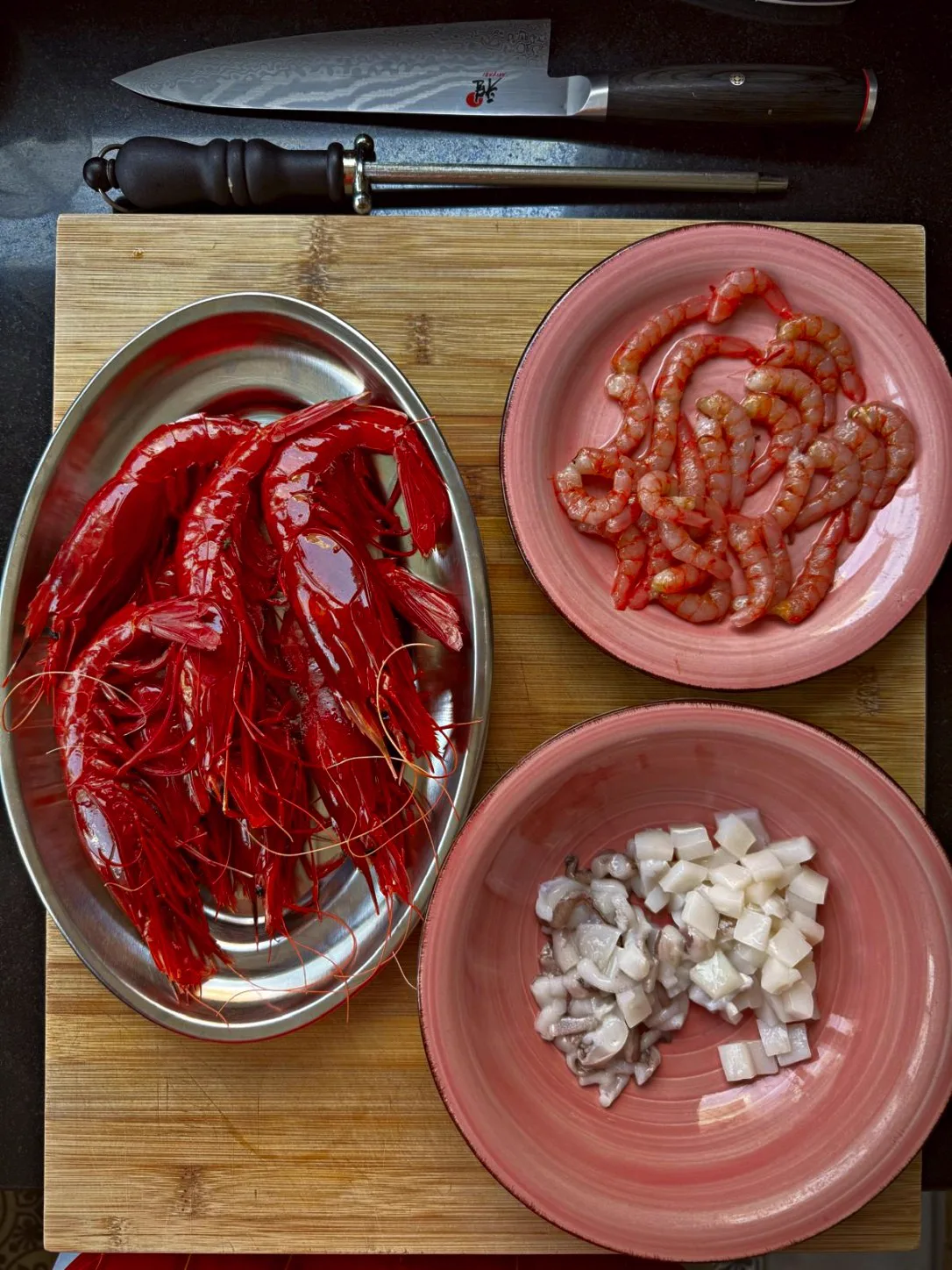 Carabinero prawns, peeled prawns and diced cuttlefish on a board, next to the knife, before cooking
